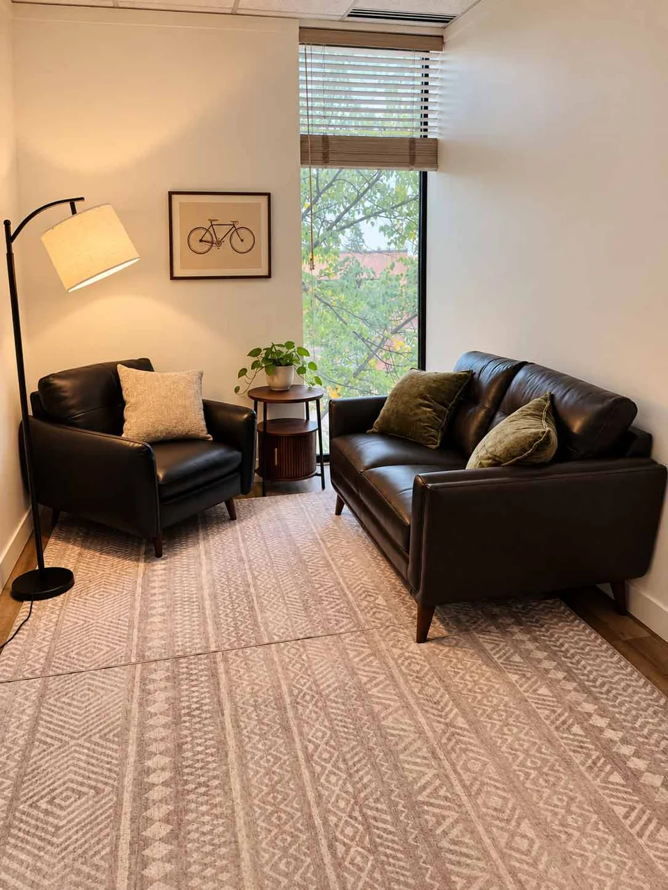 A therapy room with a dark leather sofa and armchair beside a window.